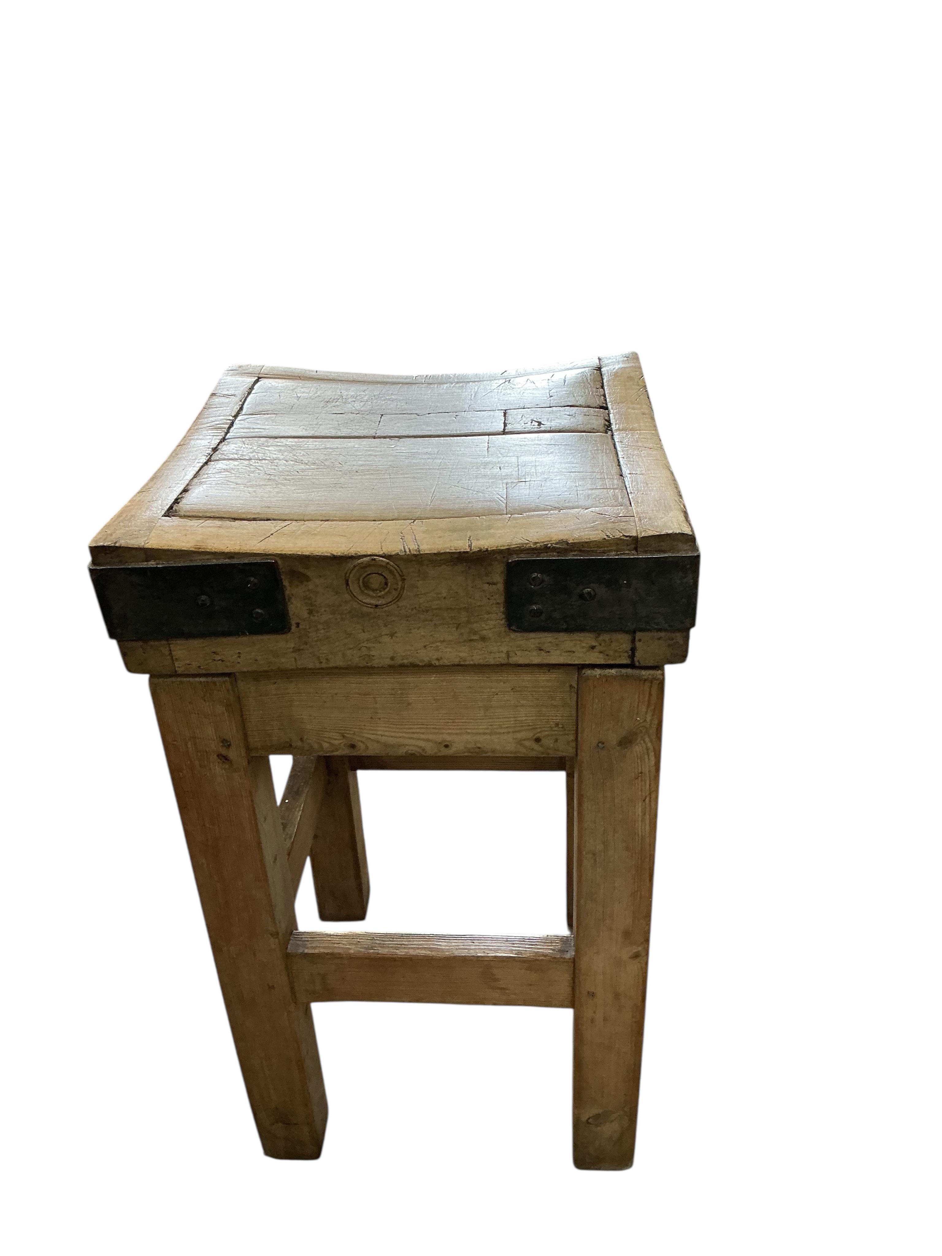A small iron bound butcher’s block on stand bears metal plaque 